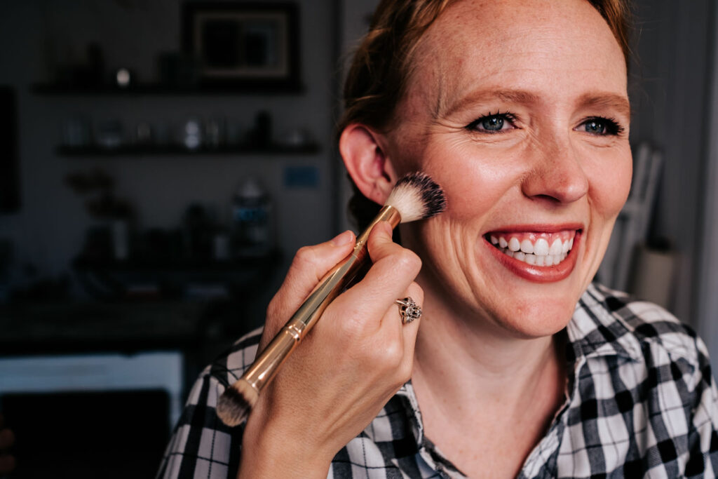 Bride with red hair getting blush put on while smiling really big