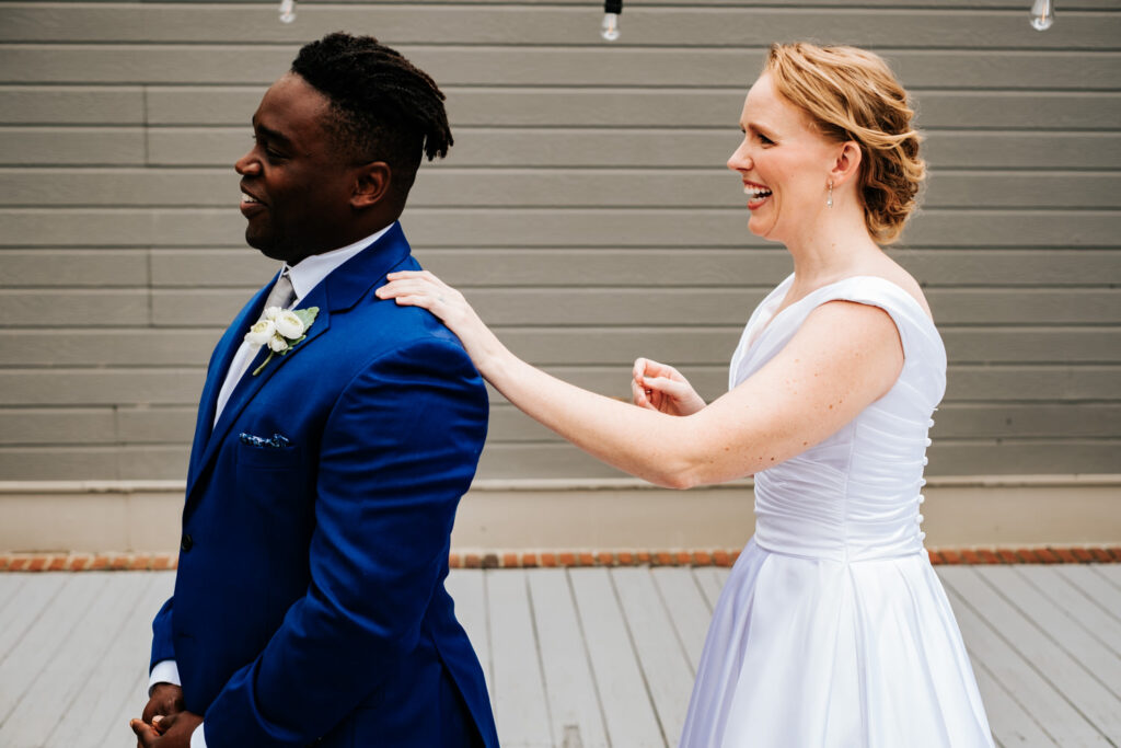 bride touching the groom's shoulder on his left side as his back is turned