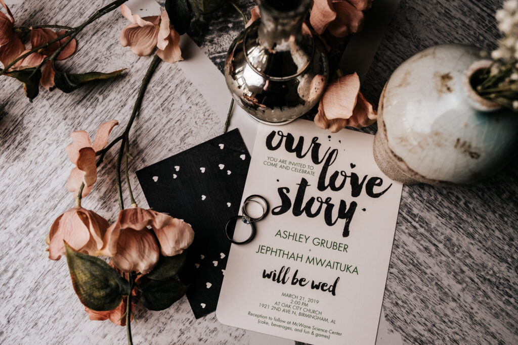 pink flowers and wedding invitation as a base on a table and wedding rings and vases on top