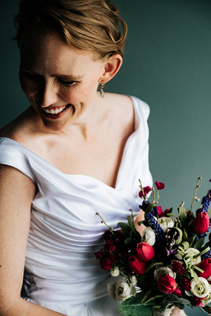 bride looking down while standing in front of a window with her bouquet